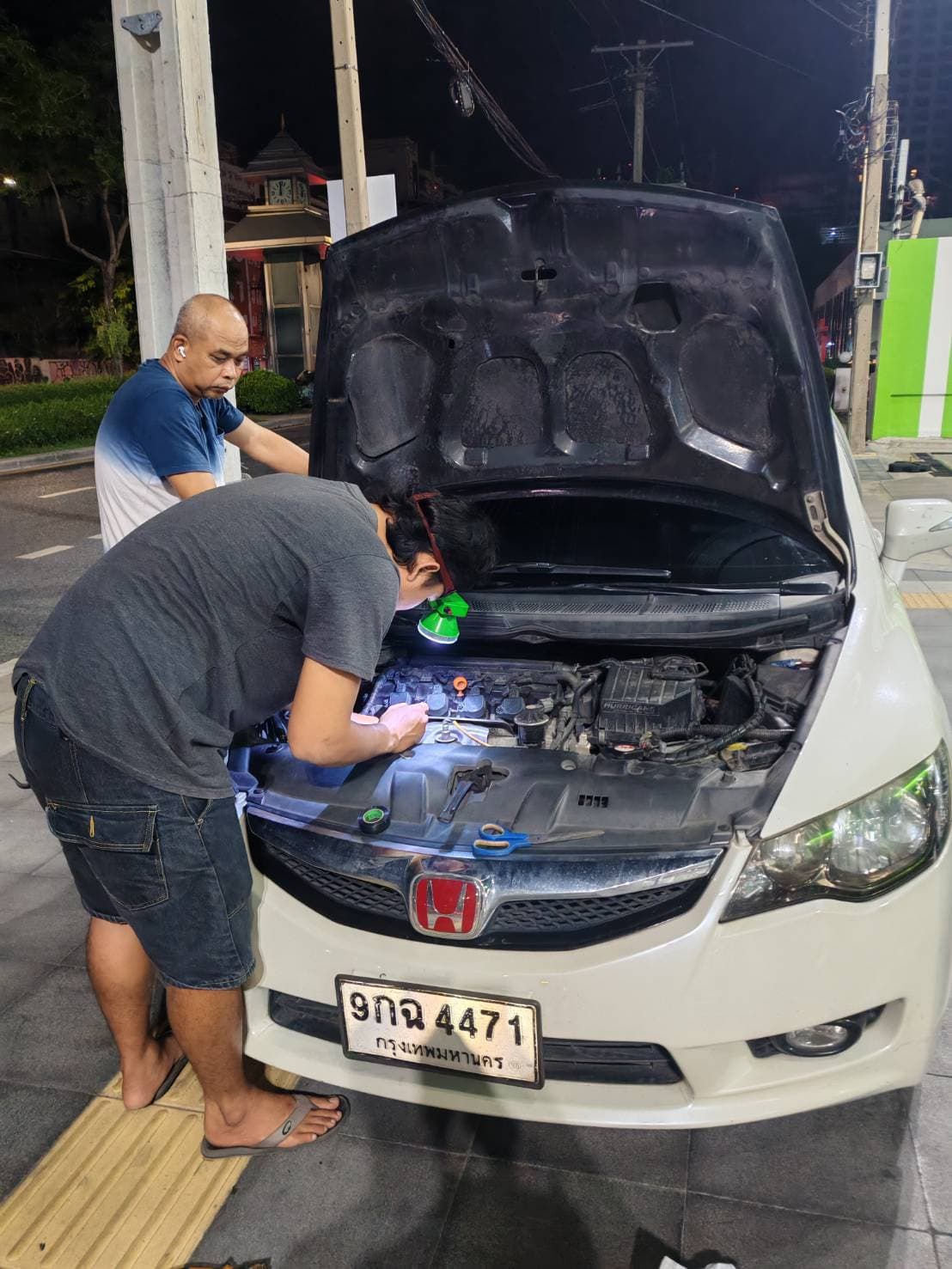 ช่างกำลังตรวจเช็กแบตเตอรี่รถยนต์ในเวลากลางคืน